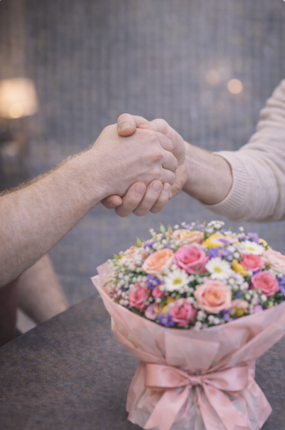 due persone che si stringono le mani in segno di riconciliazione con un bouquet di fiori sul tavolo